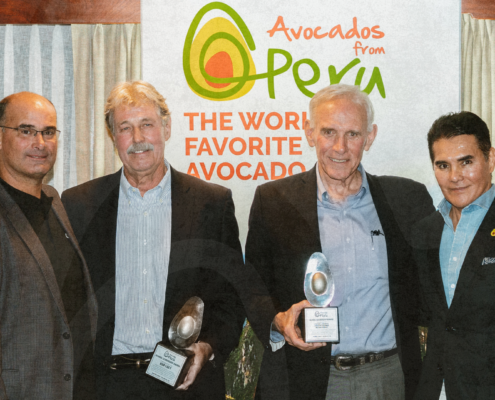 Four men pose at an Avocados from Peru event while two hold award plaques in front of a branded backdrop.