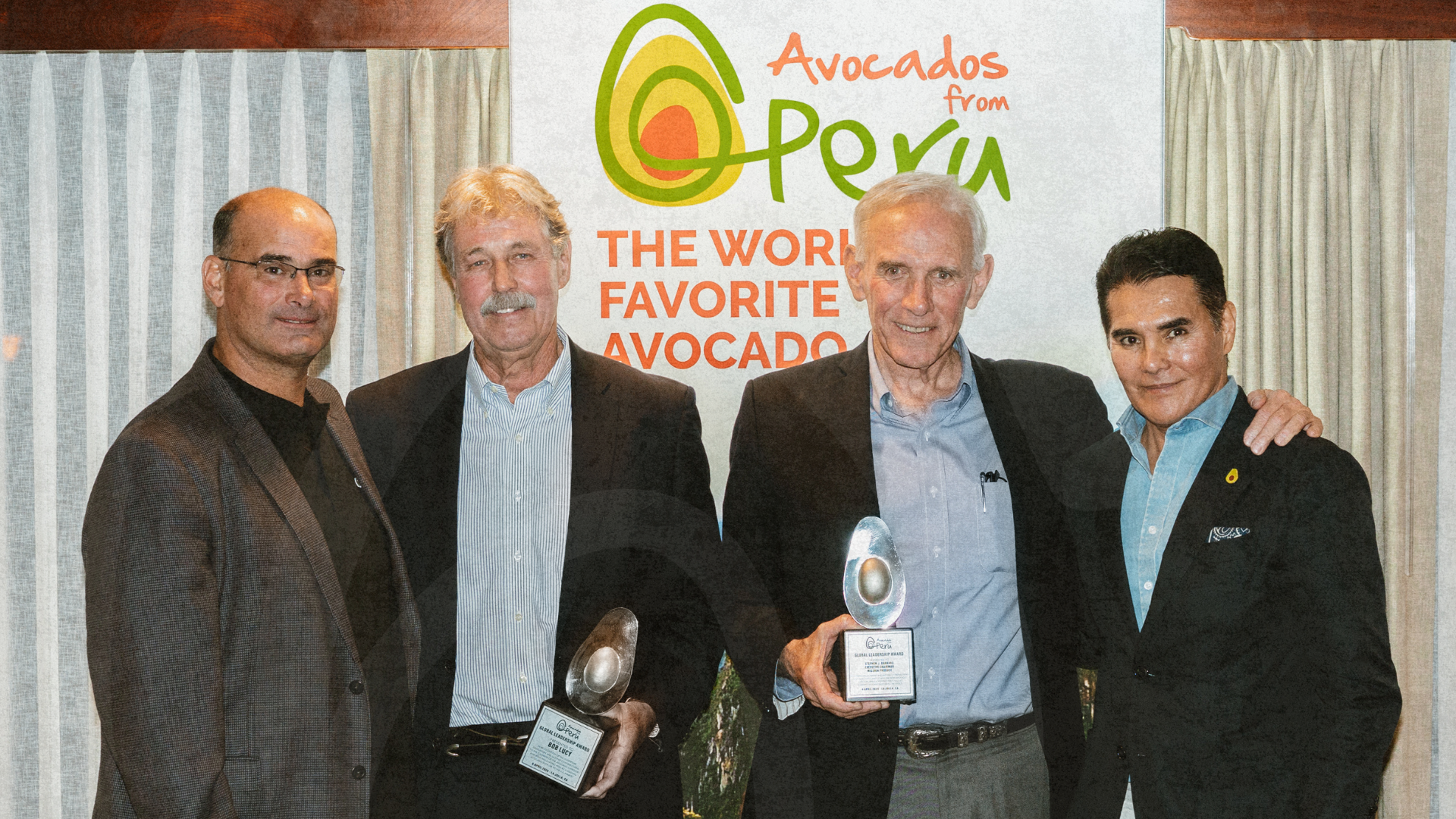 Four men pose at an Avocados from Peru event while two hold award plaques in front of a branded backdrop.